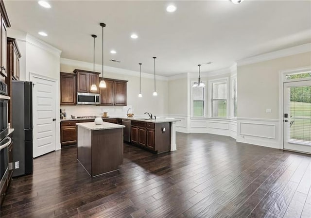 kitchen with dark brown cabinets, appliances with stainless steel finishes, decorative light fixtures, and a center island with sink