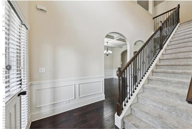 foyer entrance with dark hardwood / wood-style floors, a towering ceiling, beamed ceiling, coffered ceiling, and an inviting chandelier