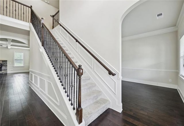 staircase featuring crown molding, a towering ceiling, wood-type flooring, and beam ceiling