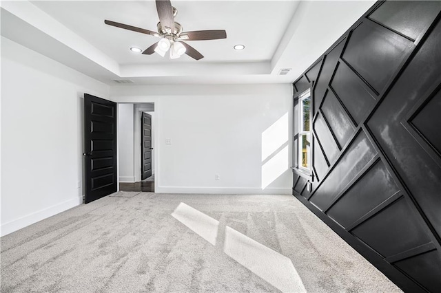 empty room featuring light carpet, a tray ceiling, and ceiling fan