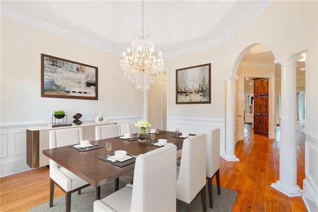 dining room with ornate columns, arched walkways, light wood finished floors, and a wainscoted wall