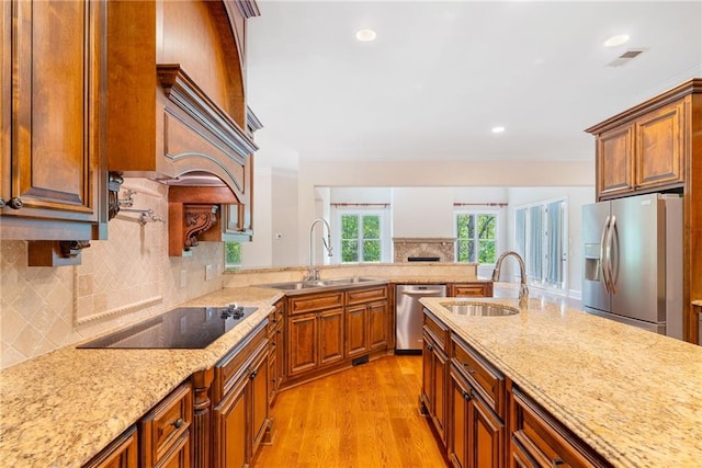 kitchen featuring appliances with stainless steel finishes, light wood-type flooring, a sink, and light stone countertops