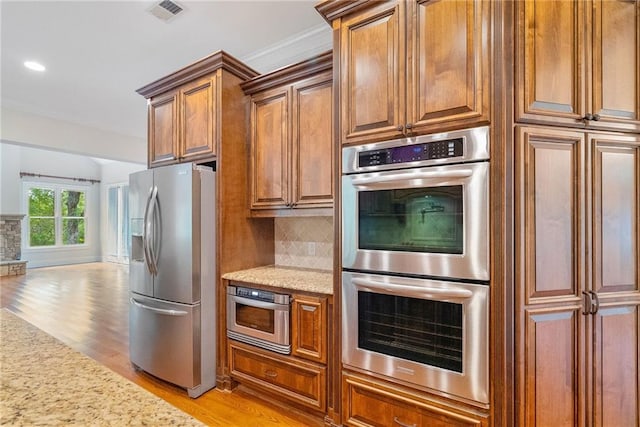 kitchen with tasteful backsplash, visible vents, light wood-style flooring, appliances with stainless steel finishes, and brown cabinetry