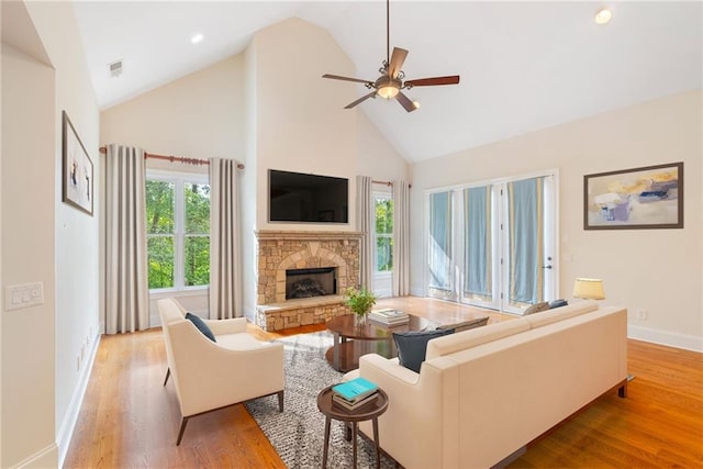 living area featuring ceiling fan, high vaulted ceiling, a stone fireplace, light wood-style flooring, and visible vents