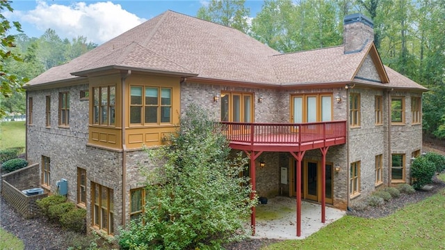 rear view of property featuring brick siding, a yard, a chimney, a shingled roof, and a patio area