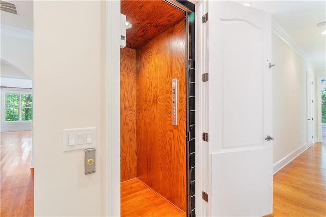 hall with ornamental molding, light wood-style flooring, and visible vents