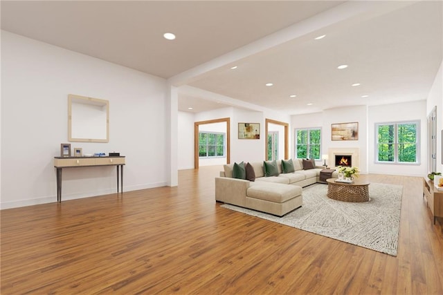 living area with a warm lit fireplace, baseboards, wood finished floors, and recessed lighting