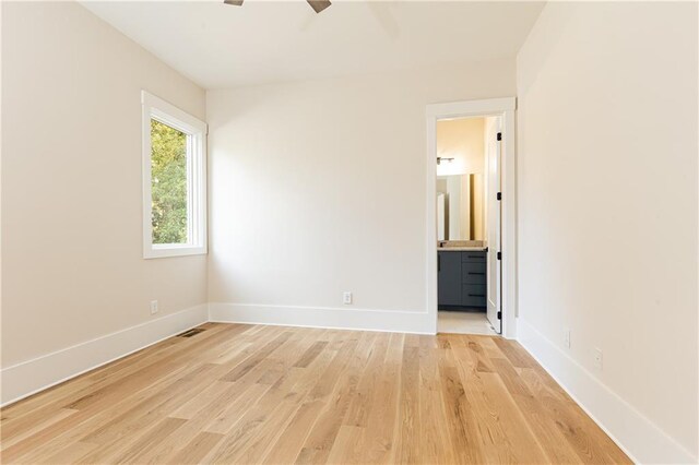 unfurnished bedroom featuring ensuite bath, light wood-type flooring, and ceiling fan