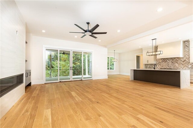 unfurnished living room with light wood-type flooring, a large fireplace, ceiling fan, and sink