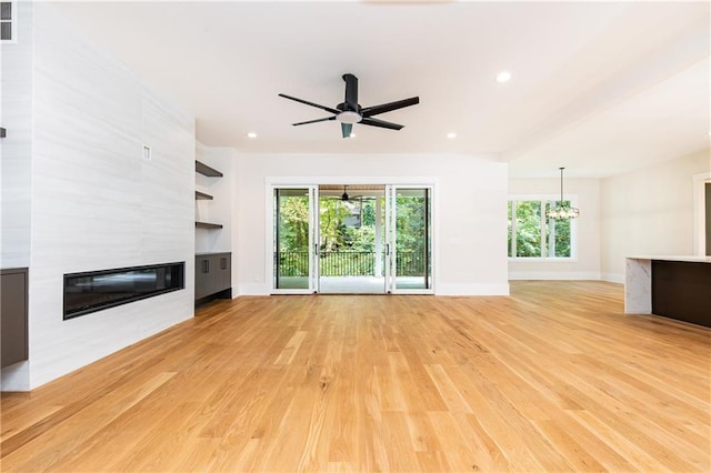 unfurnished living room featuring a large fireplace, ceiling fan with notable chandelier, a wealth of natural light, and light hardwood / wood-style flooring