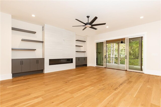 unfurnished living room with a large fireplace, ceiling fan, and light hardwood / wood-style flooring