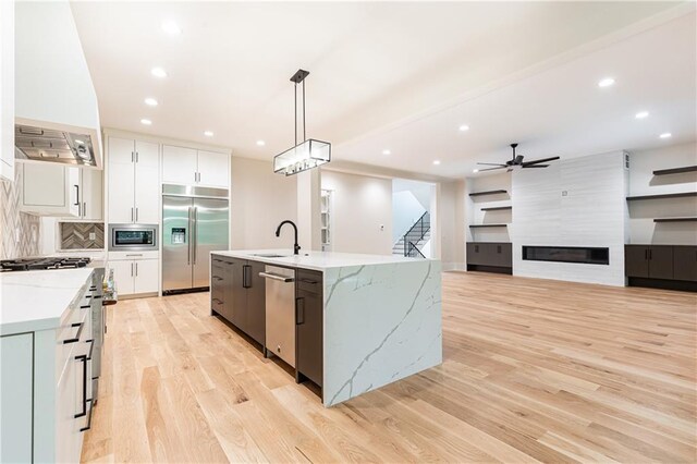 kitchen with a fireplace, white cabinetry, built in appliances, pendant lighting, and a kitchen island with sink