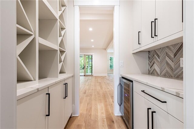 bar featuring beverage cooler, light stone countertops, white cabinetry, and light hardwood / wood-style flooring