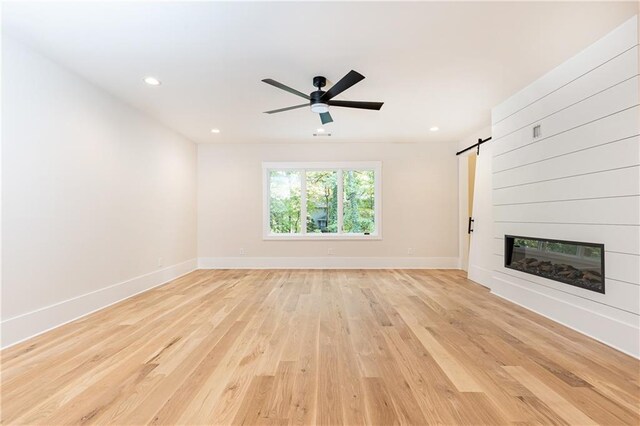 unfurnished living room featuring a barn door, ceiling fan, a fireplace, and light hardwood / wood-style flooring