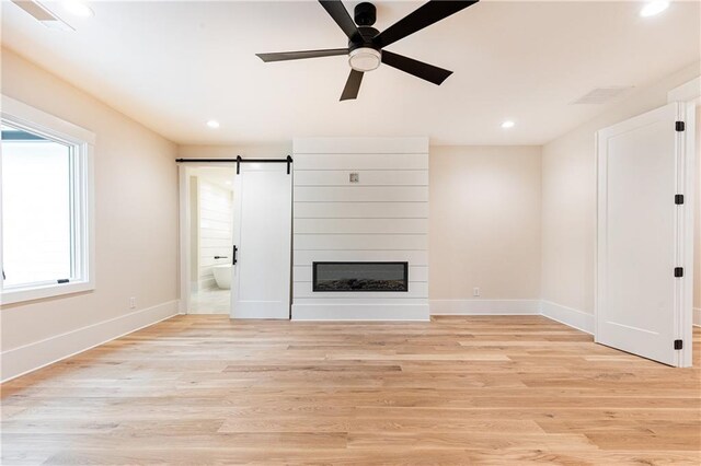 unfurnished living room with a barn door, a large fireplace, ceiling fan, and light hardwood / wood-style flooring