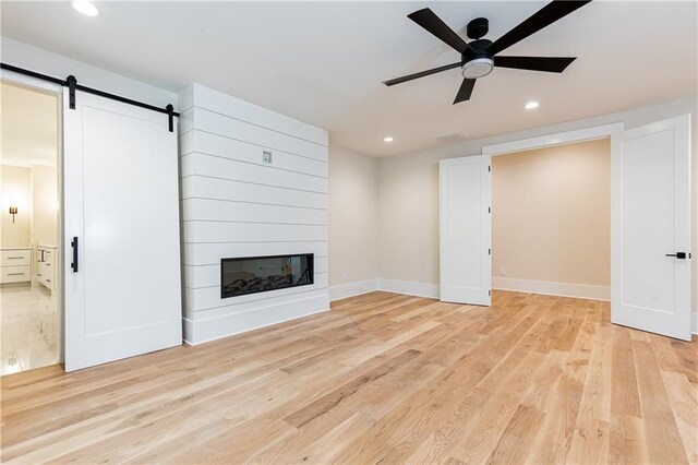 unfurnished living room featuring a barn door, ceiling fan, light hardwood / wood-style flooring, and a large fireplace