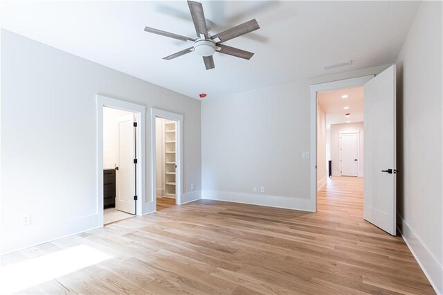 unfurnished bedroom featuring light hardwood / wood-style flooring, ceiling fan, a closet, a walk in closet, and ensuite bathroom