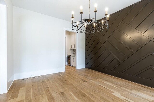 unfurnished room with light wood-type flooring, an inviting chandelier, and beverage cooler