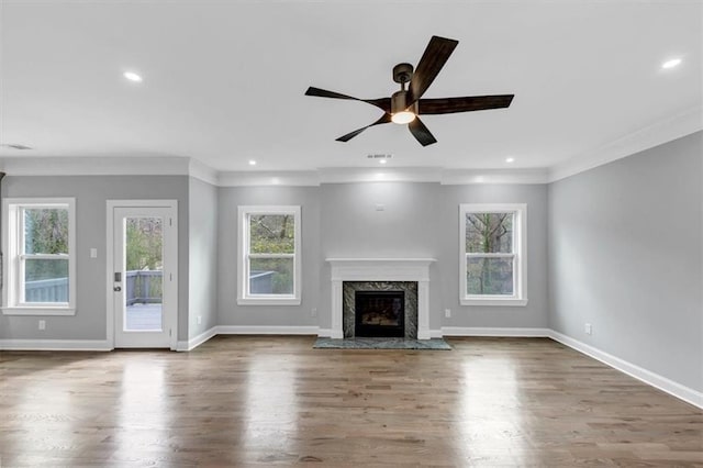 unfurnished living room with wood finished floors, visible vents, baseboards, a premium fireplace, and crown molding