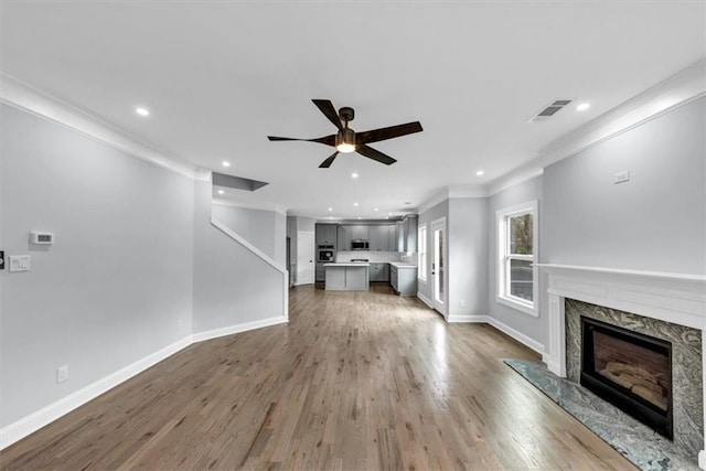 unfurnished living room with a ceiling fan, wood finished floors, visible vents, baseboards, and a fireplace