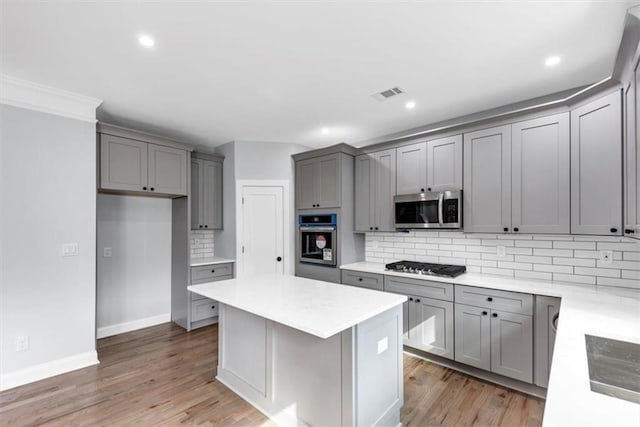 kitchen with light wood-style flooring, gray cabinetry, decorative backsplash, stainless steel appliances, and a center island