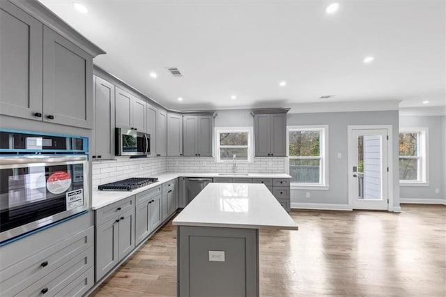 kitchen featuring tasteful backsplash, gray cabinetry, a kitchen island, light wood-type flooring, and appliances with stainless steel finishes