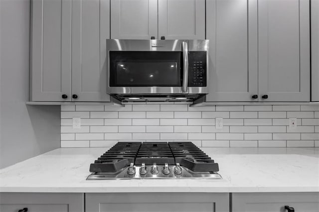 details featuring tasteful backsplash, gray cabinets, stainless steel appliances, and light stone countertops