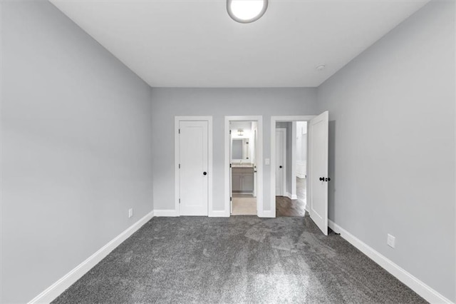 unfurnished bedroom featuring baseboards, dark colored carpet, and ensuite bathroom