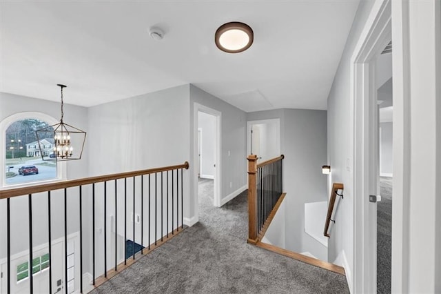 corridor featuring carpet, a notable chandelier, an upstairs landing, and baseboards