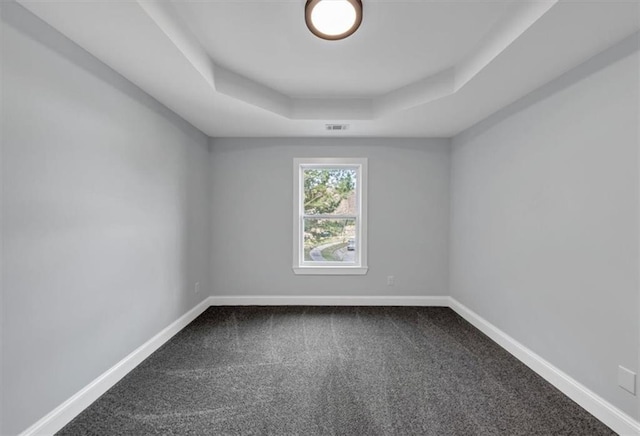 spare room featuring dark colored carpet, a tray ceiling, and baseboards