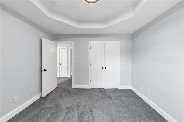 unfurnished bedroom with a tray ceiling, baseboards, carpet, and a closet