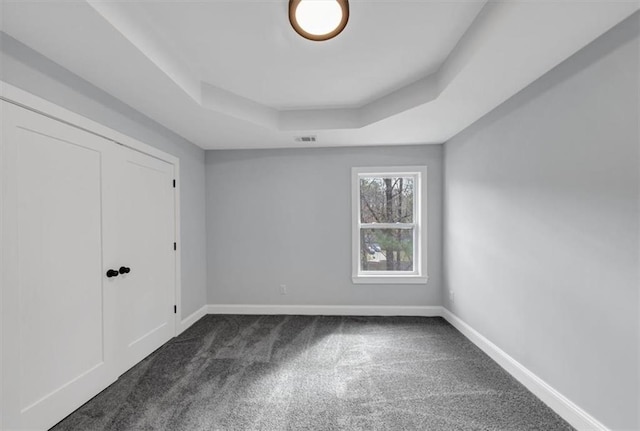 unfurnished bedroom with visible vents, dark carpet, a raised ceiling, and baseboards