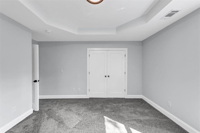 unfurnished bedroom with visible vents, a tray ceiling, a closet, carpet, and baseboards