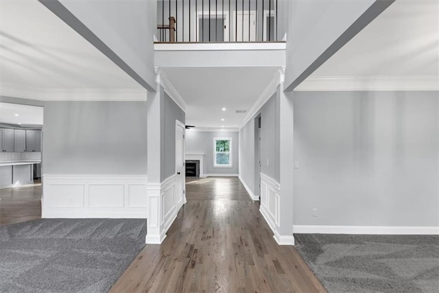 entryway featuring a wainscoted wall, ornamental molding, a fireplace, wood finished floors, and a decorative wall