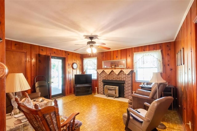 living room featuring crown molding, wood walls, a ceiling fan, and a fireplace