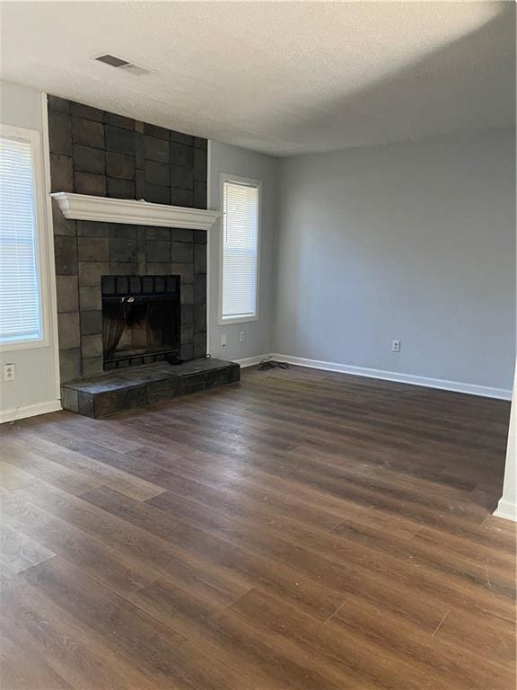 unfurnished living room with dark hardwood / wood-style flooring, a healthy amount of sunlight, a textured ceiling, and a fireplace