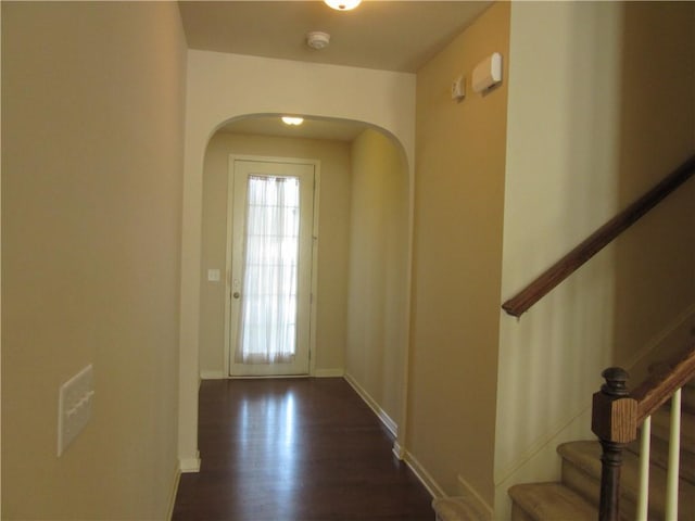 entryway with dark wood-style floors, stairway, arched walkways, and baseboards