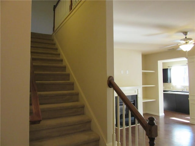 staircase with wood finished floors, a ceiling fan, and baseboards