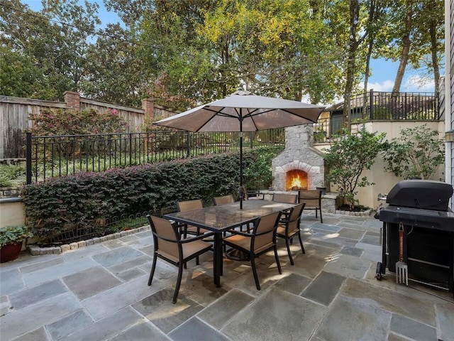 view of patio / terrace with a fenced backyard, an outdoor stone fireplace, grilling area, and outdoor dining space