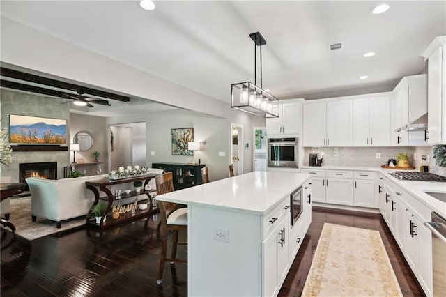 kitchen featuring white cabinets, hanging light fixtures, appliances with stainless steel finishes, dark wood-type flooring, and a center island