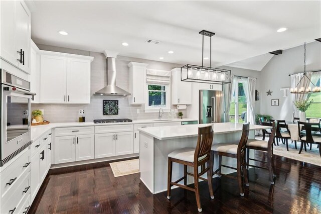 kitchen featuring wall chimney range hood, appliances with stainless steel finishes, white cabinetry, dark wood-type flooring, and sink