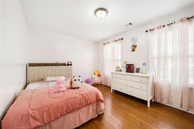 bedroom with a textured ceiling, dark wood-style floors, and visible vents