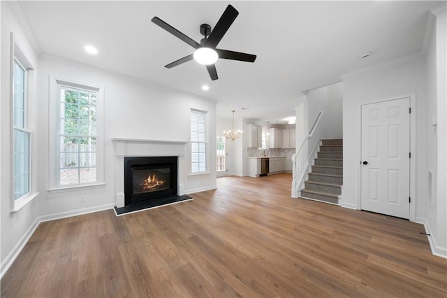 unfurnished living room featuring hardwood / wood-style flooring, ornamental molding, and ceiling fan with notable chandelier