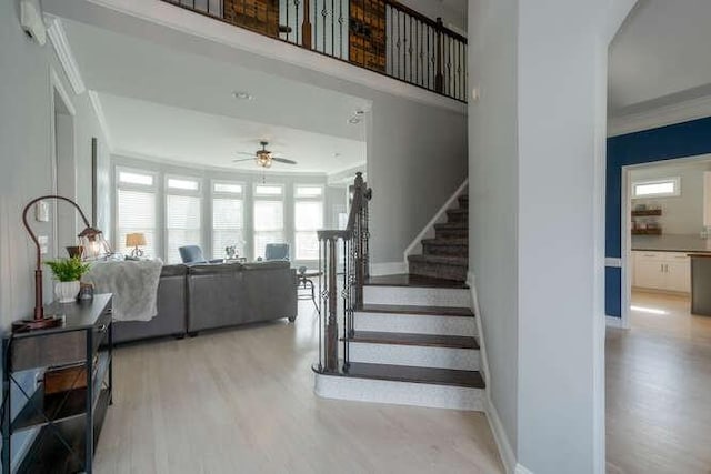 staircase featuring baseboards, a ceiling fan, crown molding, and wood finished floors