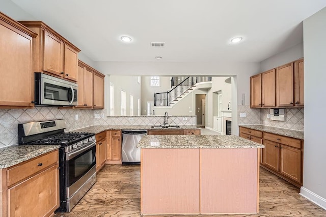 kitchen featuring light stone counters, stainless steel appliances, visible vents, a kitchen island, and a sink