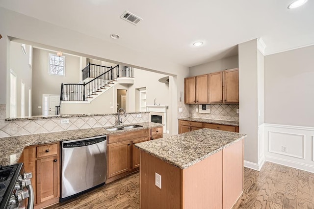 kitchen with light stone counters, a center island, stainless steel appliances, visible vents, and a sink