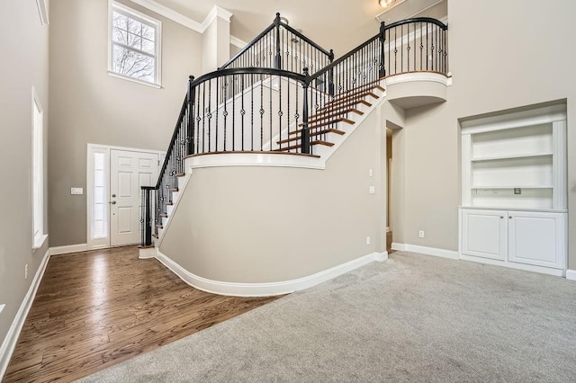 stairway featuring wood finished floors, a towering ceiling, and baseboards