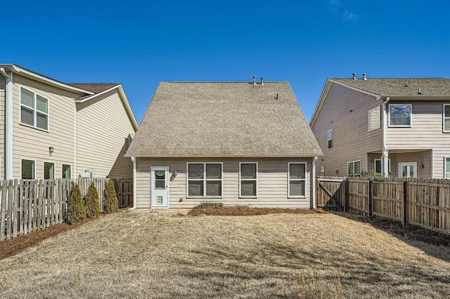 rear view of house featuring a shingled roof and a fenced backyard