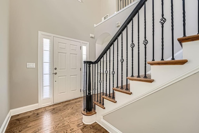 foyer entrance featuring a high ceiling, wood finished floors, visible vents, baseboards, and stairway