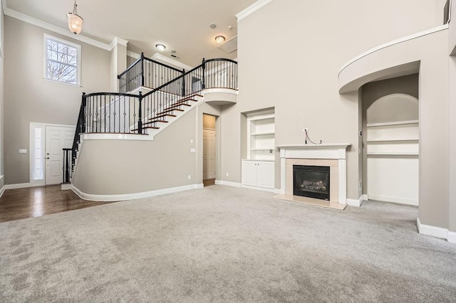 unfurnished living room with built in features, baseboards, ornamental molding, carpet, and a glass covered fireplace